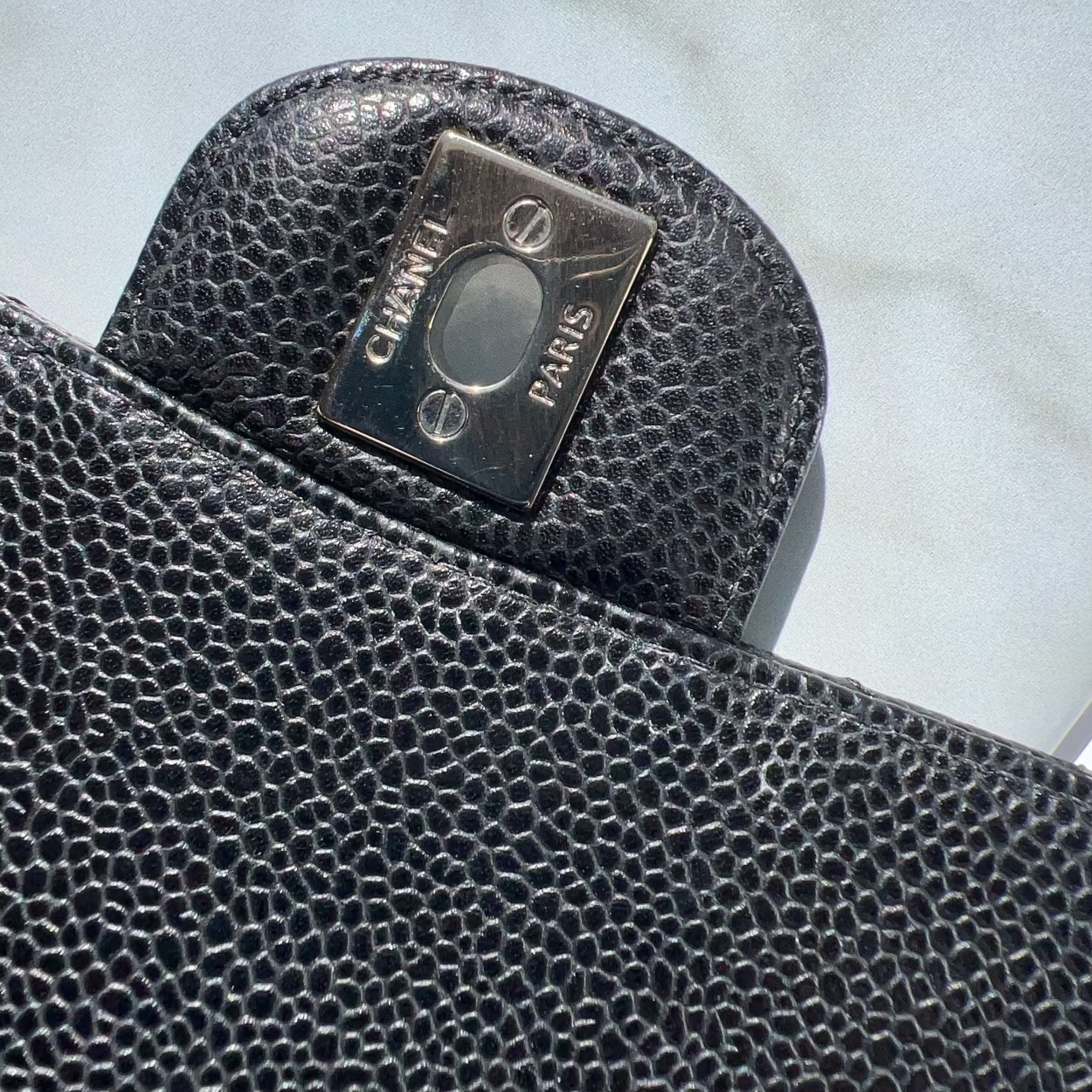 Close-up of a textured black leather product with a brand label on a light gray background
