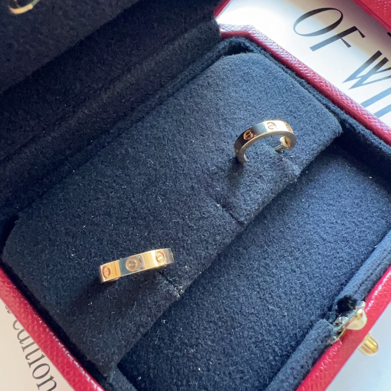 Two gold rings in a Cartier box with a red interior.