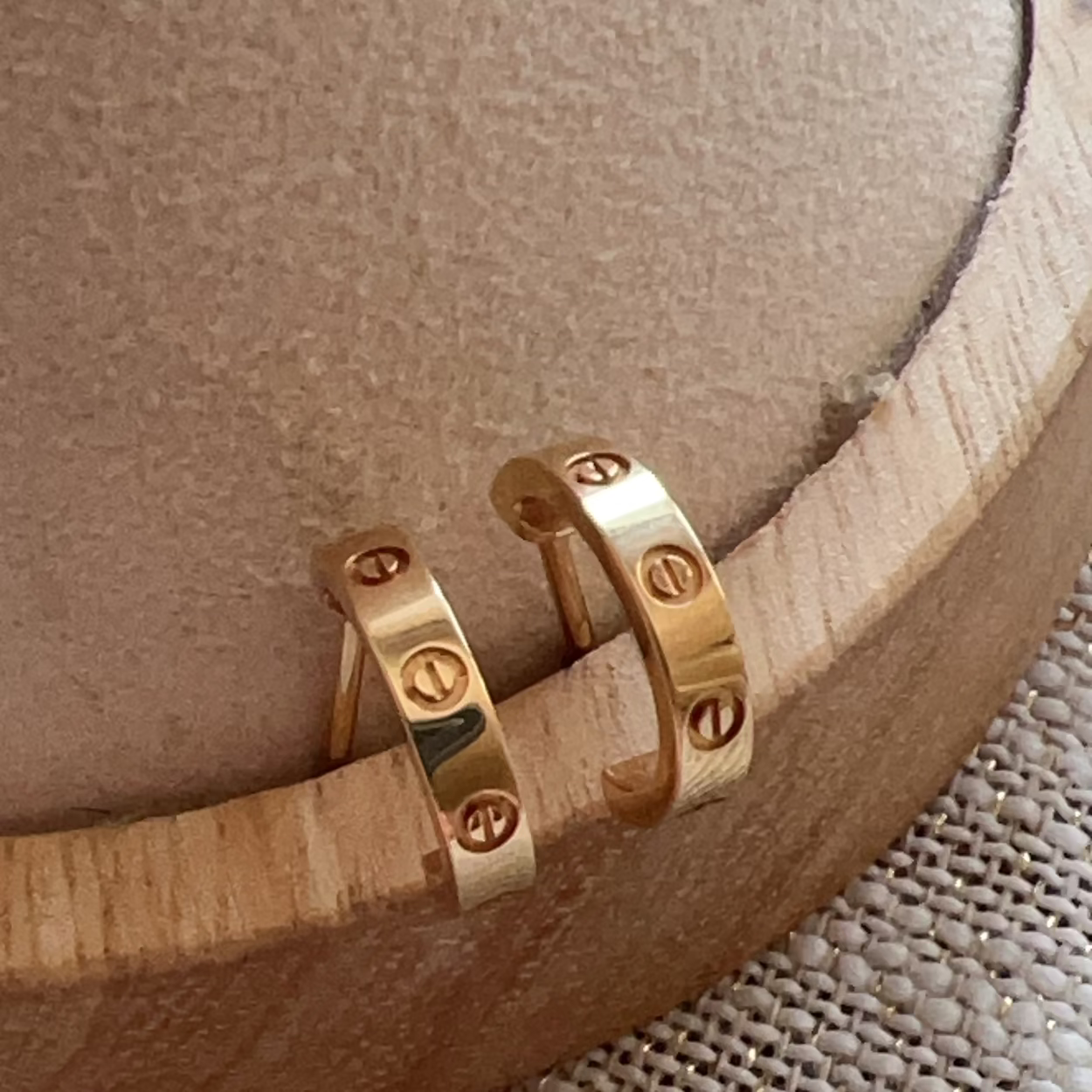 Gold hoop earrings on a wooden stand with a neutral background