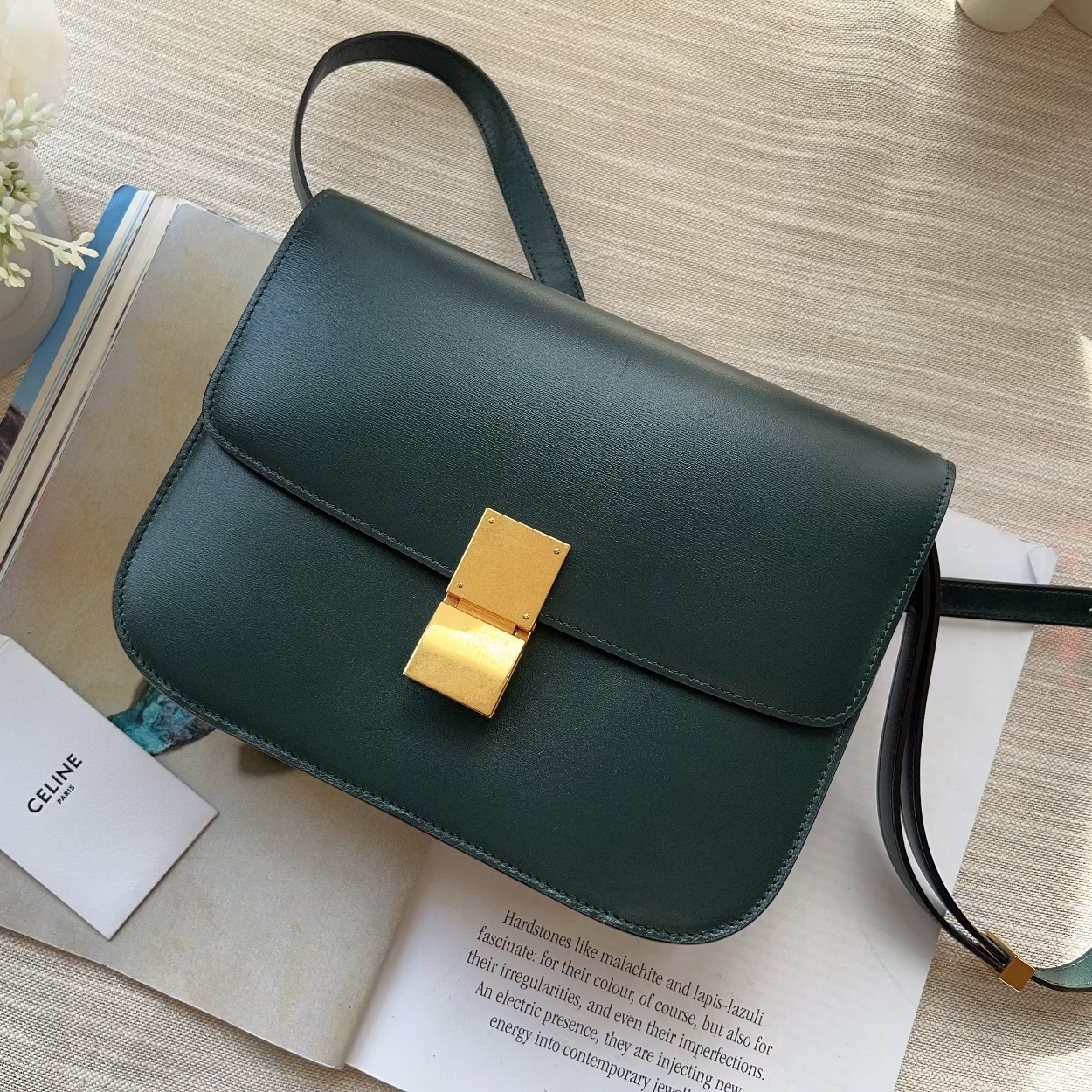 Green handbag with gold clasp on a table with books and flowers