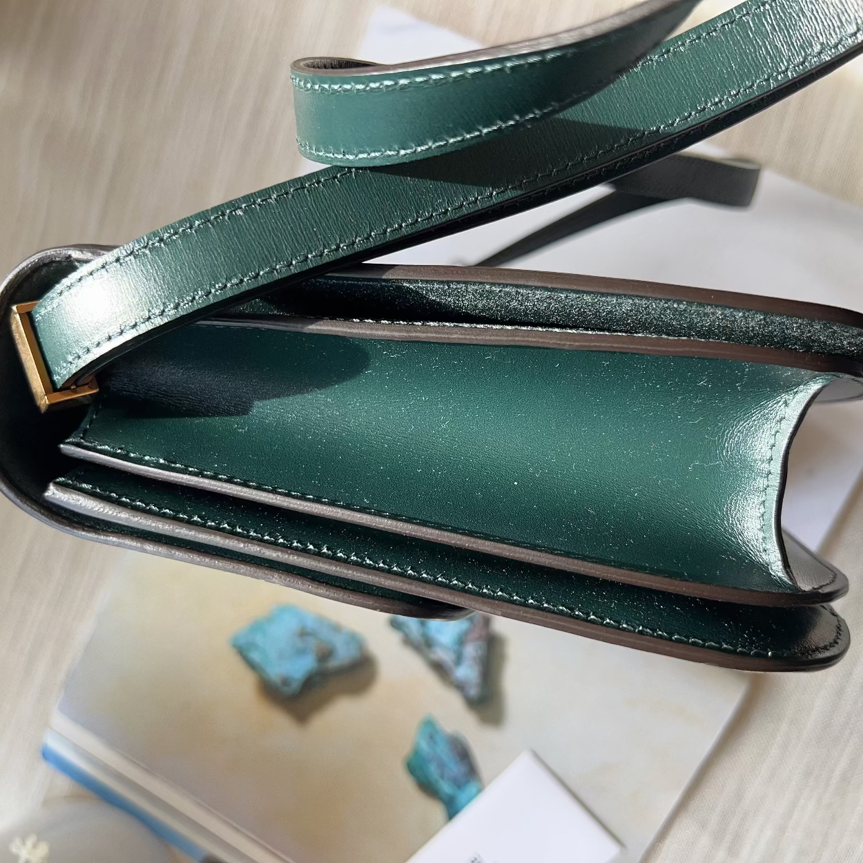 Green leather clutch bag on a light wooden surface