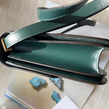Green leather clutch bag on a light wooden surface