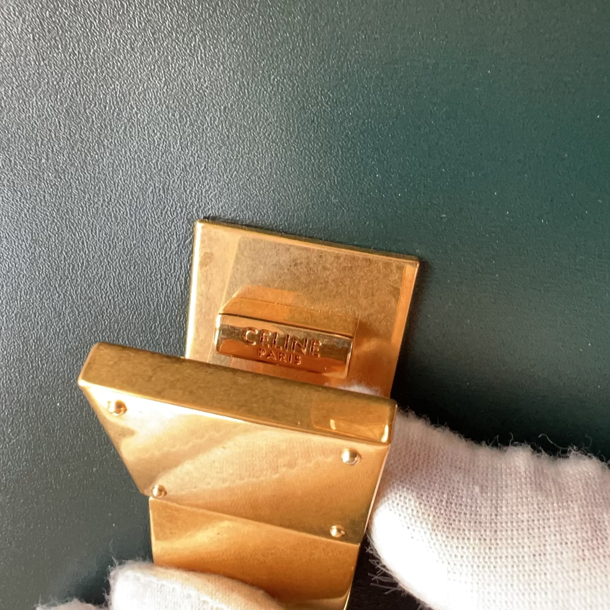 Gold belt buckle with 'Cartier' engraving held against a dark background