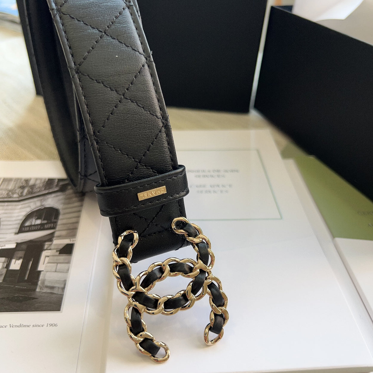 Black quilted leather belt with gold chain detail on a magazine