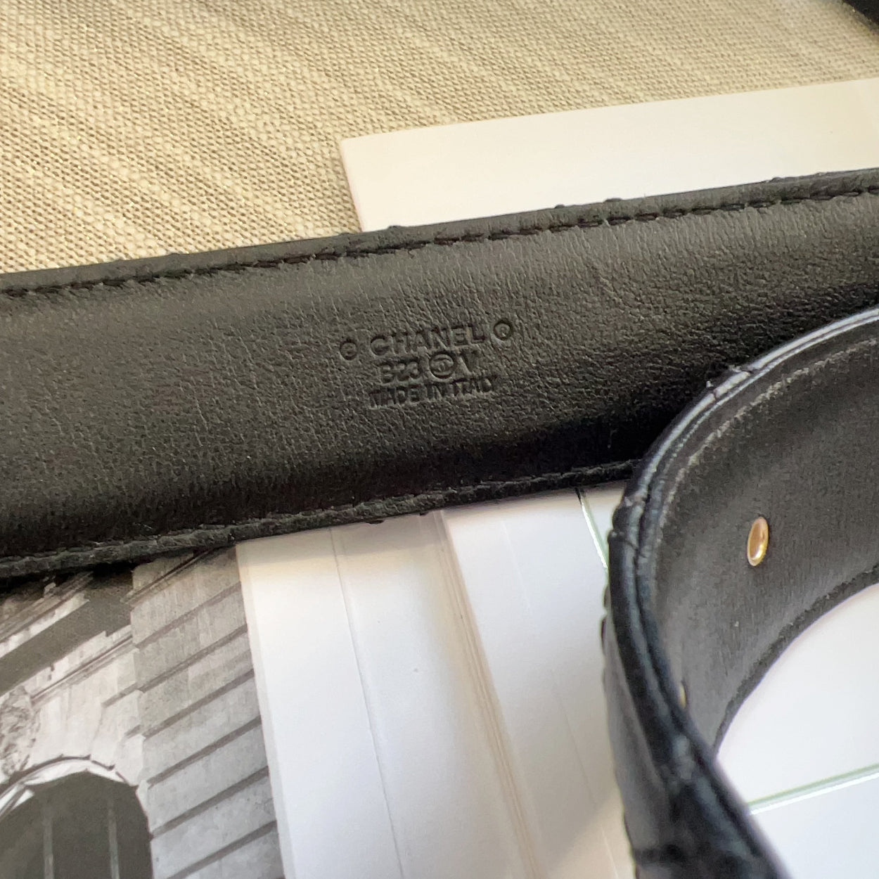 Close-up of a black Chanel belt with visible branding on a textured surface.