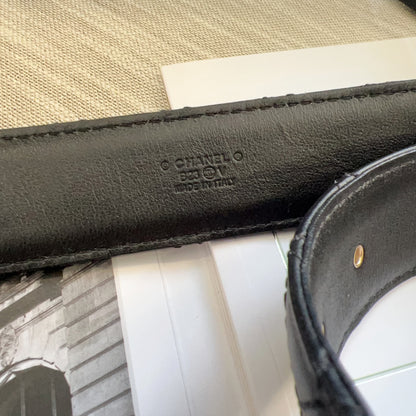 Close-up of a black Chanel belt with visible branding on a textured surface.