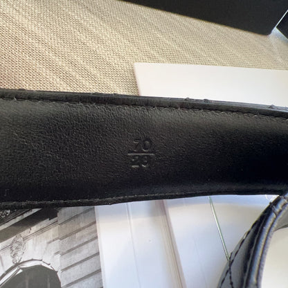 Close-up of a black leather strap with a brand logo on a textured surface.