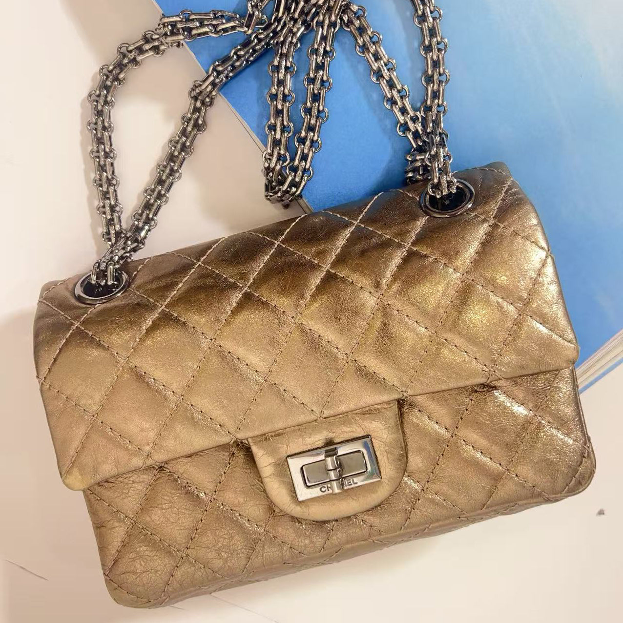 Gold quilted handbag with a chain strap on a light blue surface