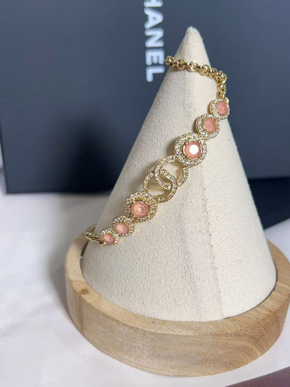 Gold bracelet with pink stones on a white cone-shaped stand with a Chanel box in the background.