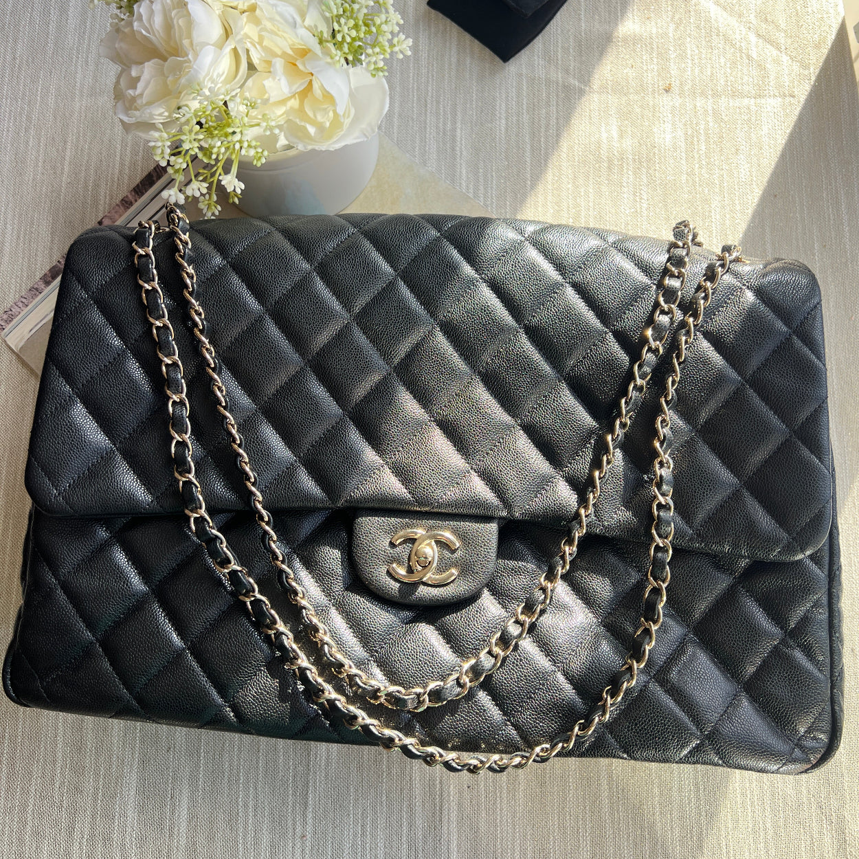 Black quilted handbag with chain strap on a wooden surface with flowers and a black box.