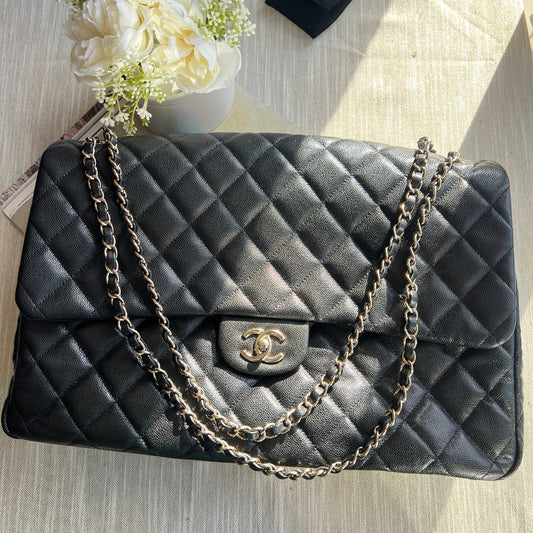 Black quilted handbag with chain strap on a wooden surface with flowers and a black box.