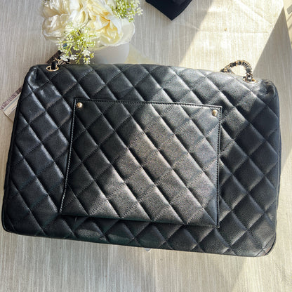 Black quilted handbag on a light wooden surface with flowers and a black box.