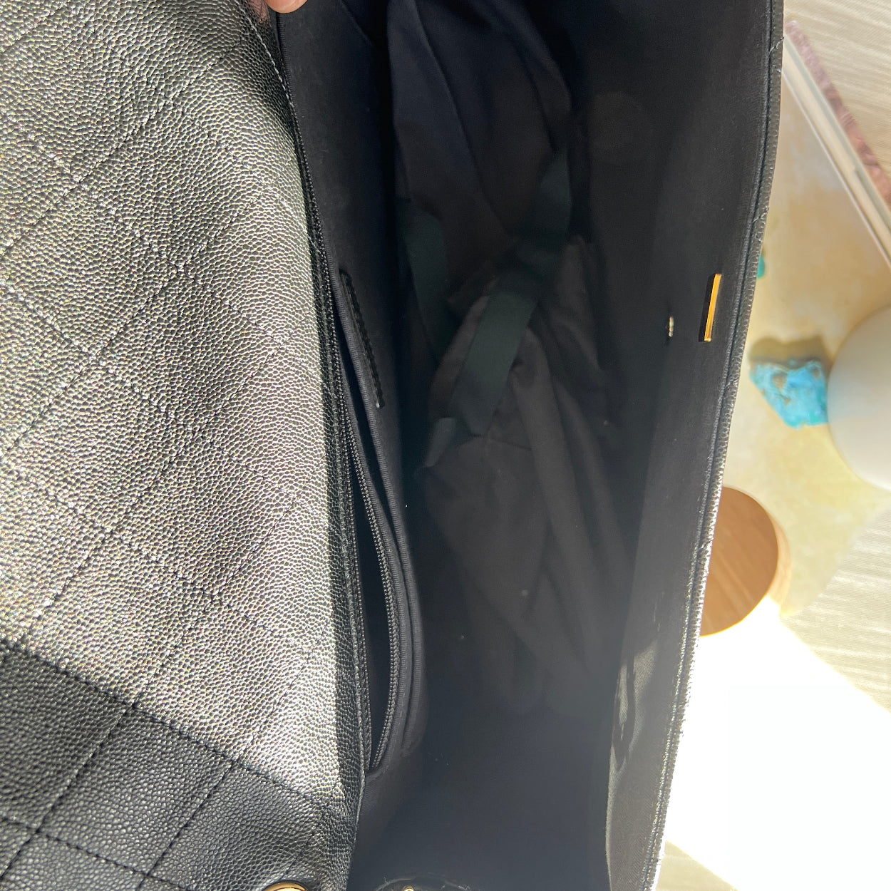 Gray quilted handbag with a hand holding open the flap, showing the interior.