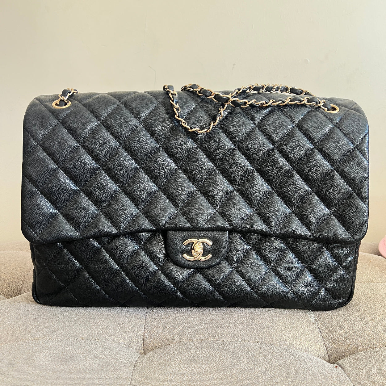 Black quilted handbag with gold chain on a beige surface