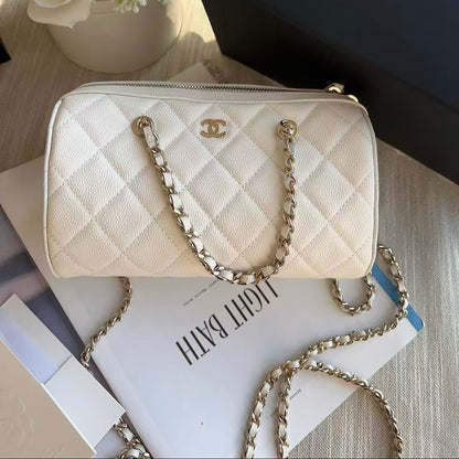 Quilted handbag with chain strap on a surface with flowers and a book in the background