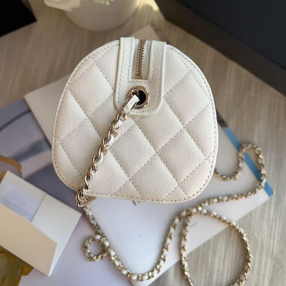Quilted cream-colored handbag with gold chain on a light wooden surface with flowers and books.