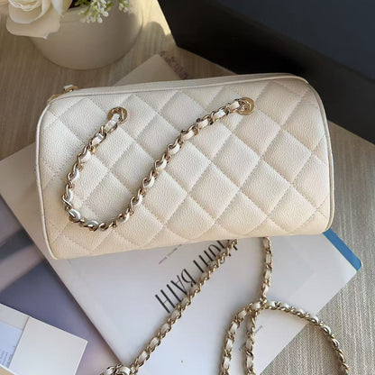 Beige quilted handbag with gold chain on a surface with flowers and books in the background