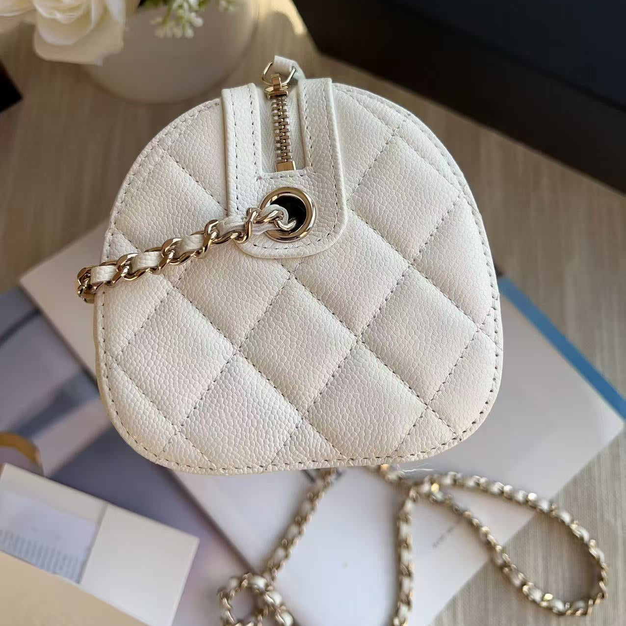 White quilted handbag with gold chain on a surface with flowers in the background