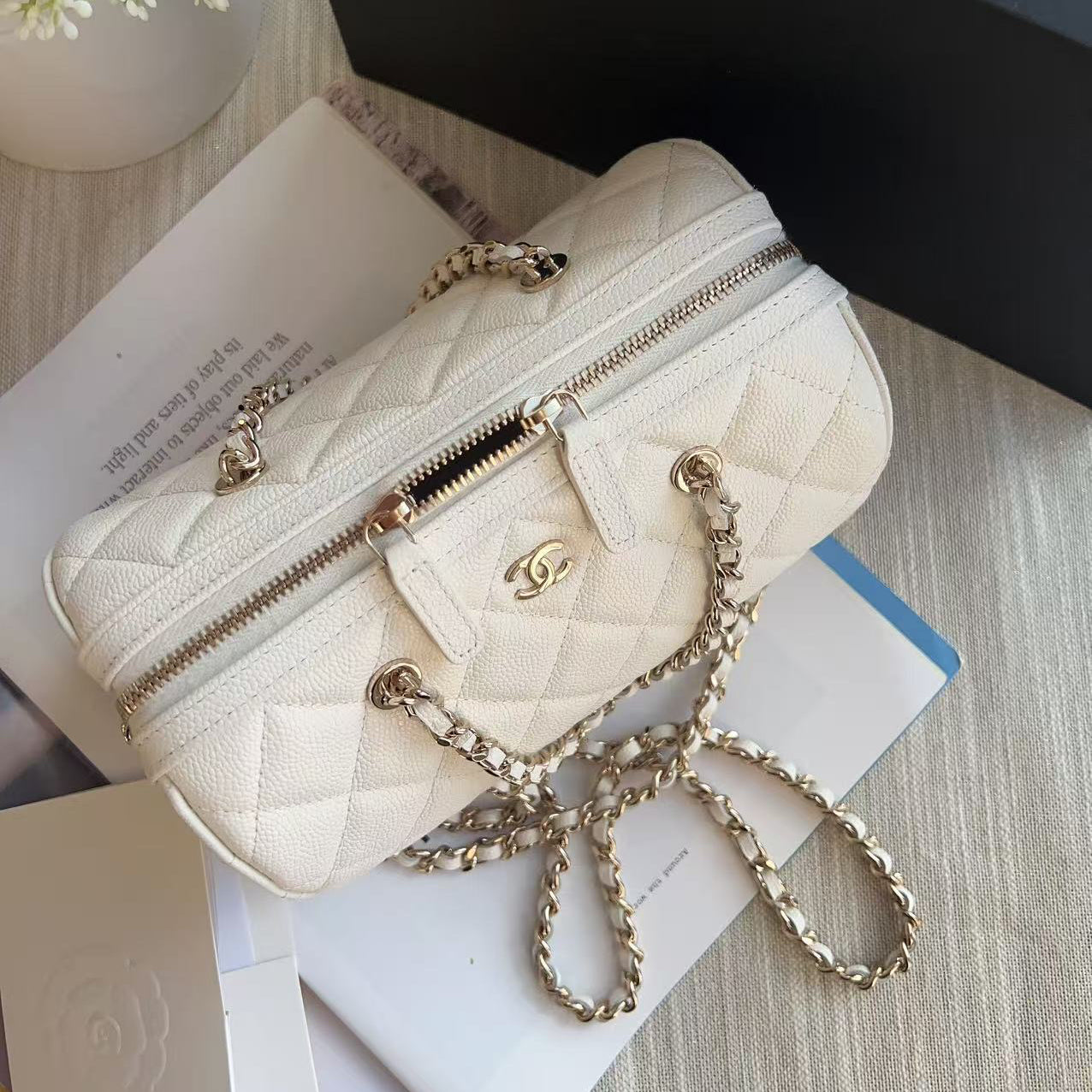 Quilted cream handbag with gold chain on a surface with books and flowers.