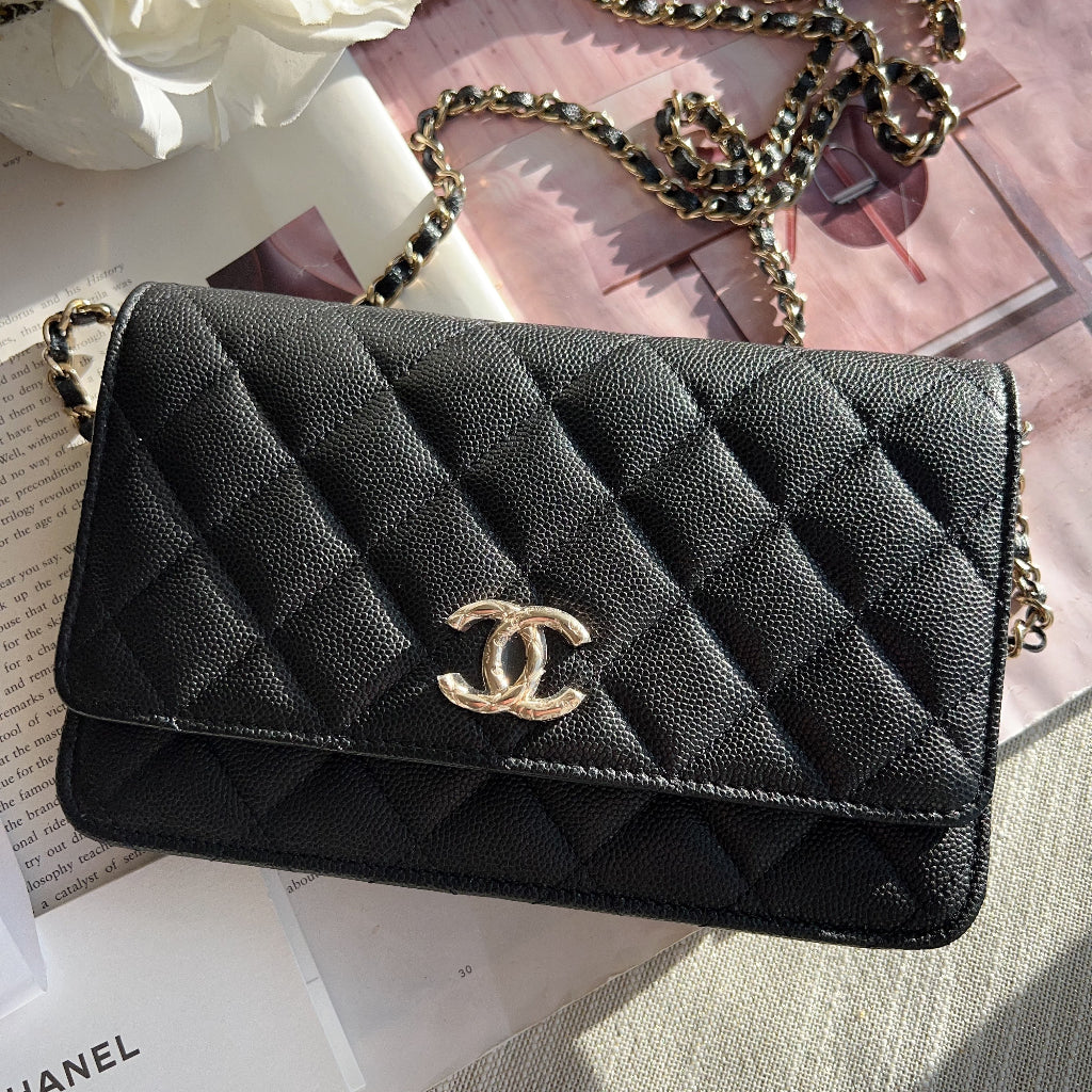 Black quilted Chanel handbag with gold chain on a surface with flowers and a book.
