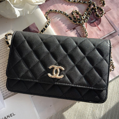 Black quilted Chanel handbag with gold chain on a surface with flowers and a book.
