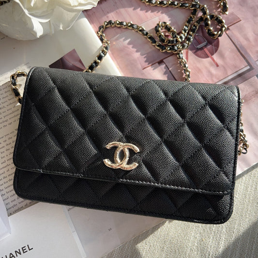 Black quilted Chanel handbag with gold chain on a surface with flowers and a book.