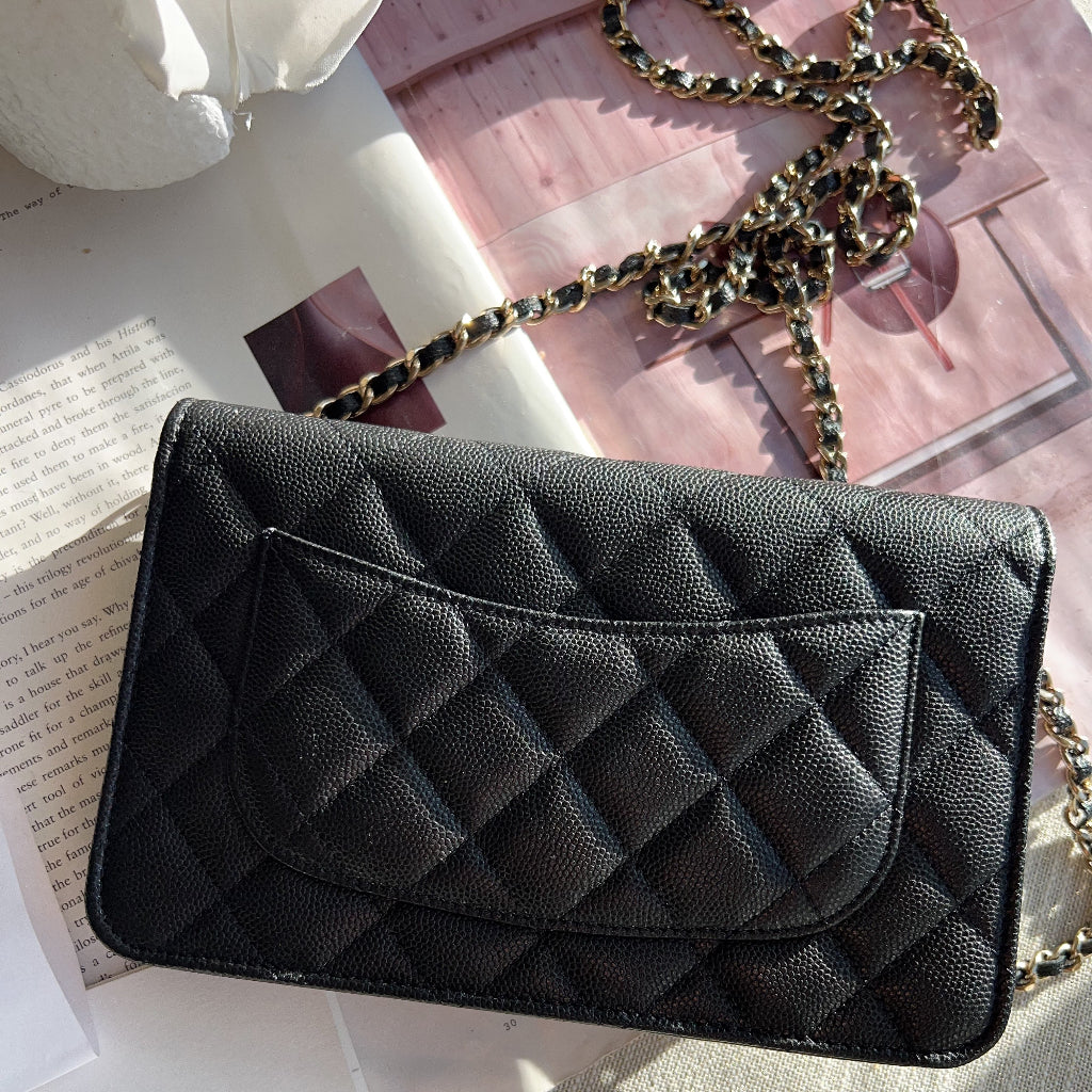 Black quilted handbag with a chain strap on a textured surface