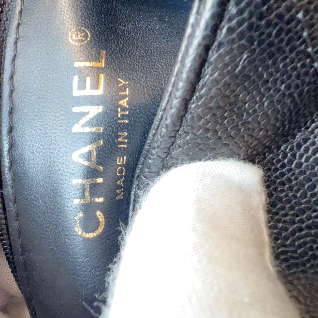 Close-up of a black leather Chanel shoe interior with gold CHANEL lettering and 'MADE IN ITALY' text, held by white-gloved hands.