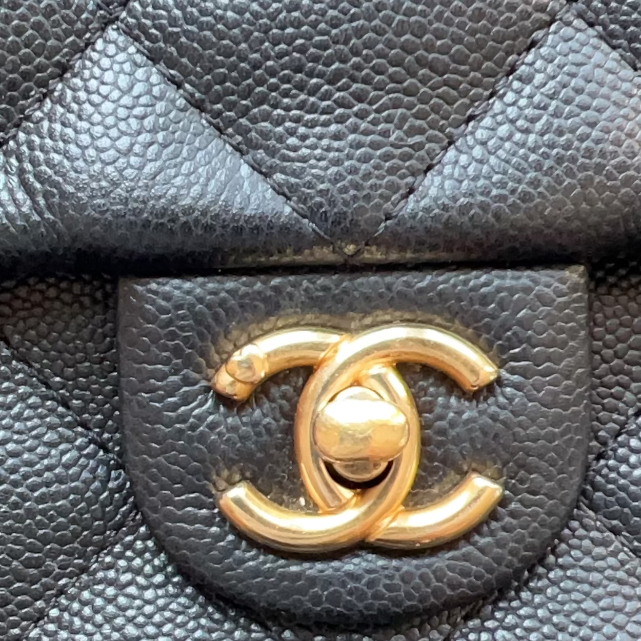 Close-up of a black quilted leather handbag with a gold-tone interlocking CC logo clasp on a textured flap.