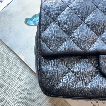 A close-up of a black quilted leather handbag resting on a textured gray fabric surface with a white paper underneath.