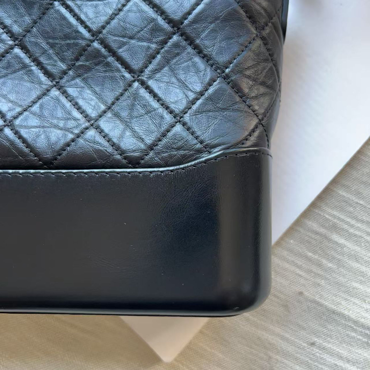Close-up of a black leather handbag showing a smooth top flap and a quilted diamond-stitched body on a white surface.