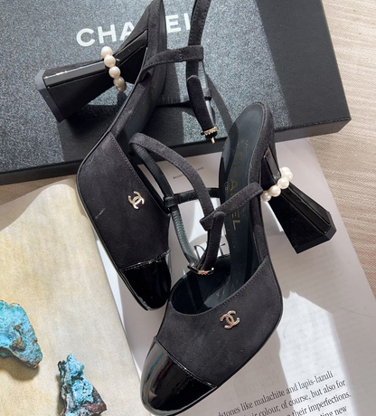 Black high-heeled shoes with pearl details on a surface with a Chanel box in the background.