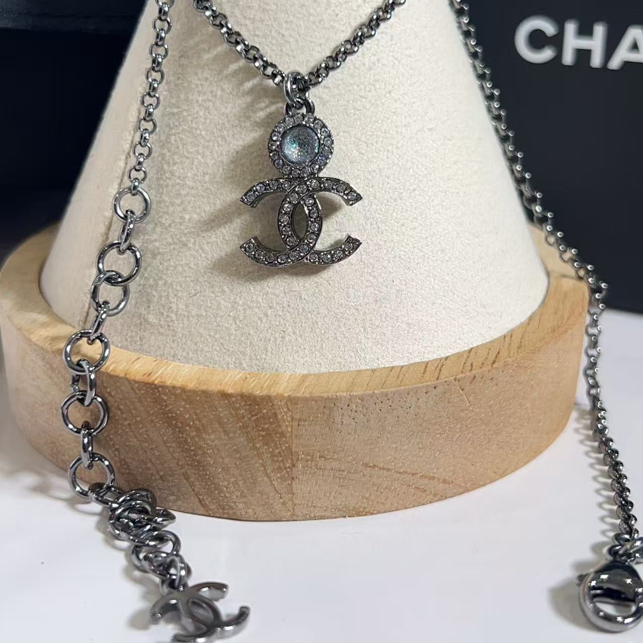 Silver necklace with pendant on a white stand with 'Chanel' branding.