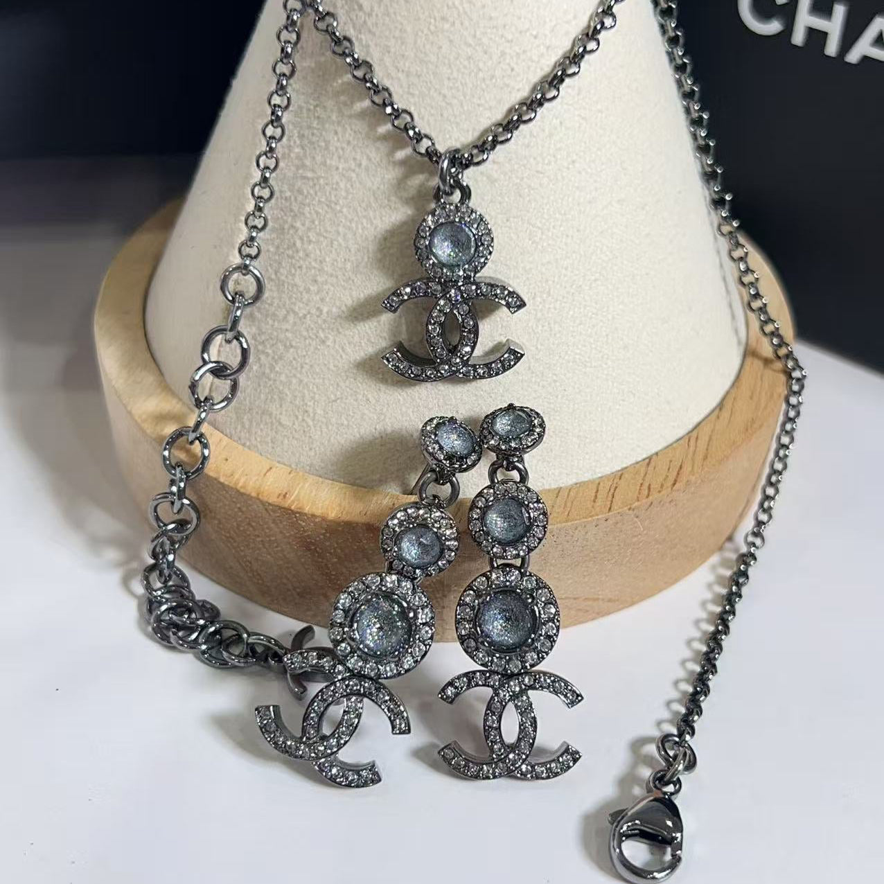 Chanel jewelry set with necklace and earrings on a wooden stand.
