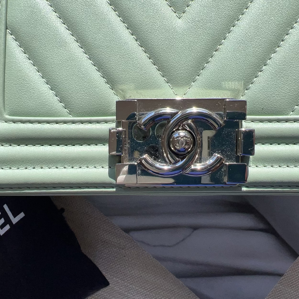 Close-up of a light green quilted handbag with a silver Chanel logo clasp.