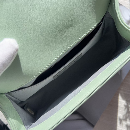 Close-up of a light green leather bag with white gloves on a wooden surface