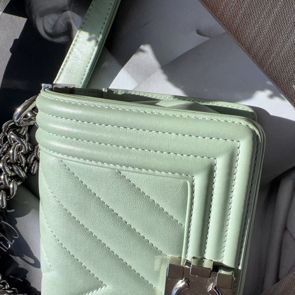Light green quilted handbag with a chain detail on a textured surface