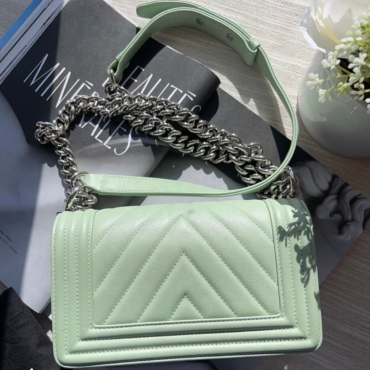 Light green handbag with chain handle on a surface with a magazine underneath