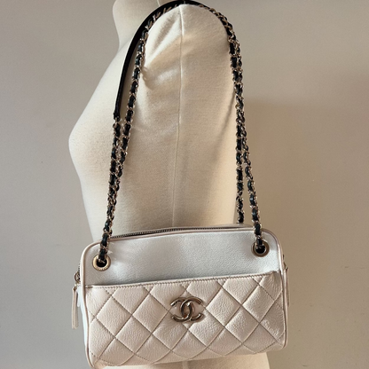 Silver quilted handbag with black chain strap on a mannequin against a neutral background