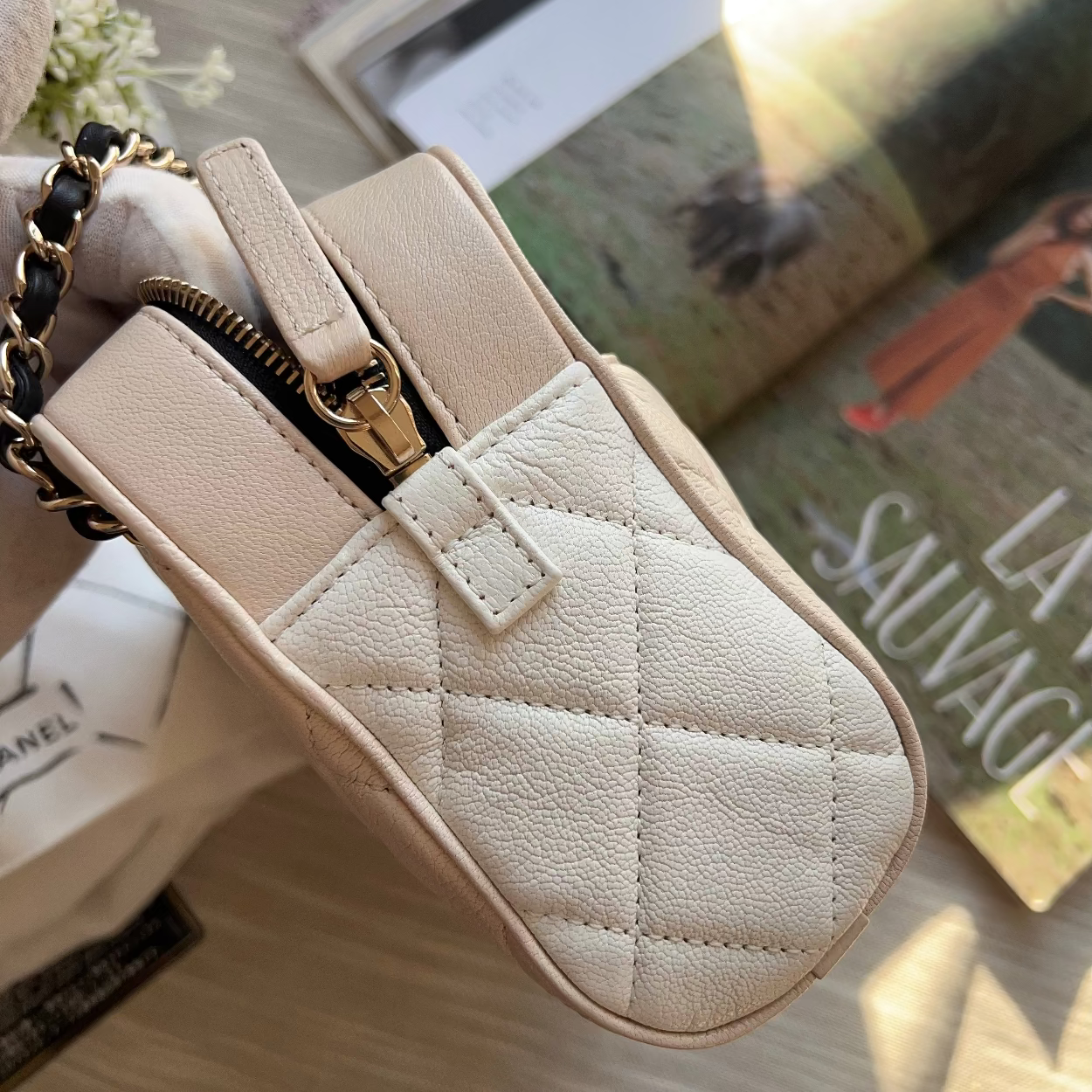 Beige quilted handbag with gold zipper on a surface with books in the background