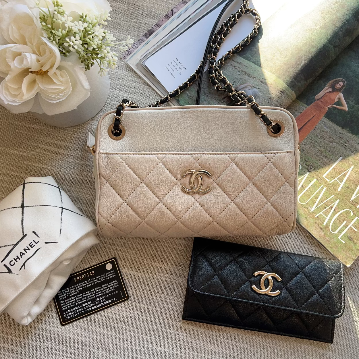 Chanel handbag and wallet on a textured surface with flowers and magazine.