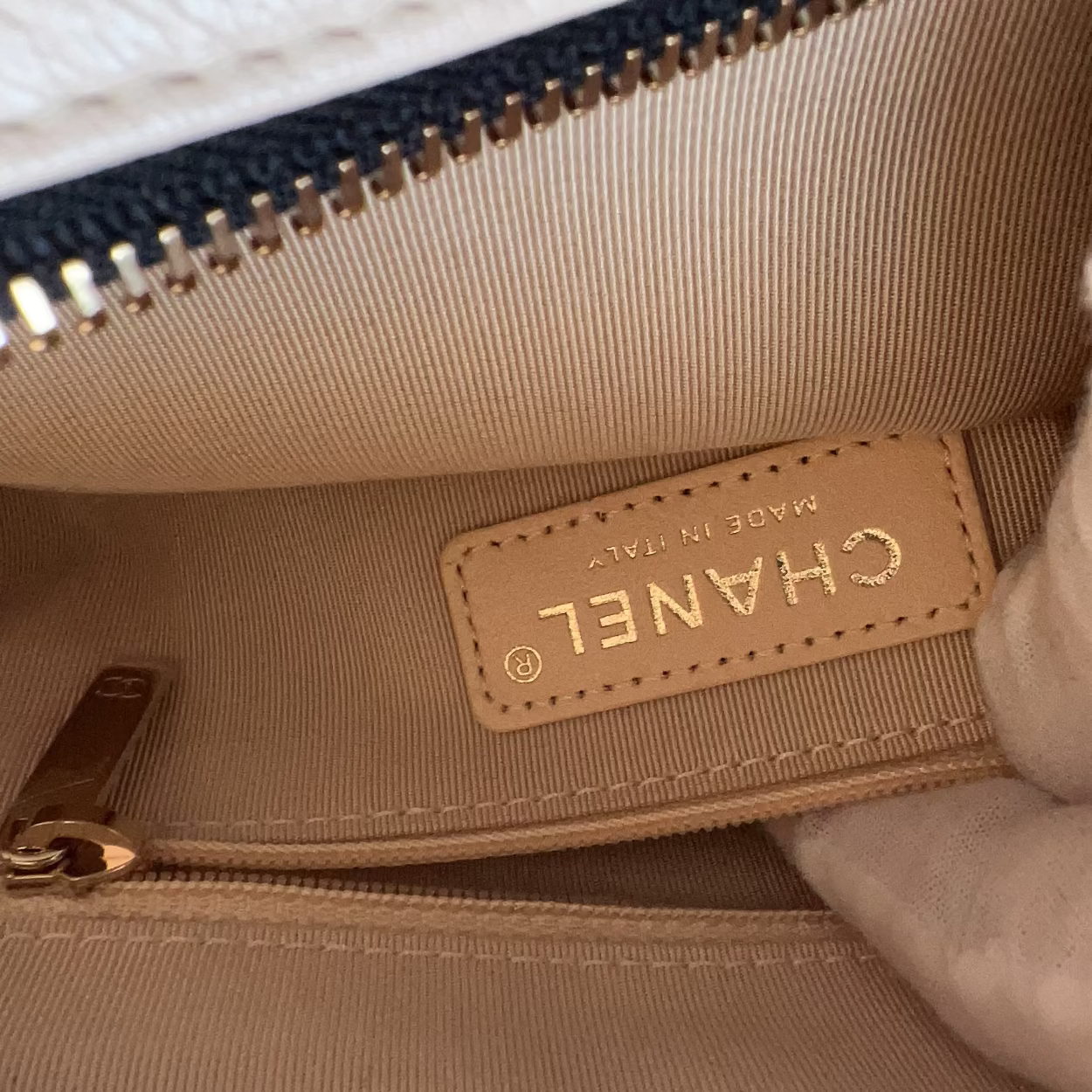 Close-up of a beige Chanel handbag with a gold zipper.