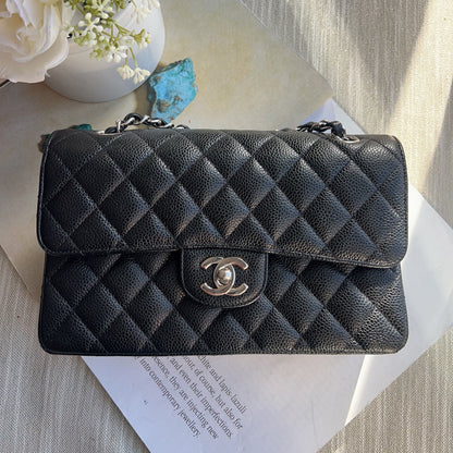 Black quilted handbag with silver clasp on a light surface with flowers and paper.