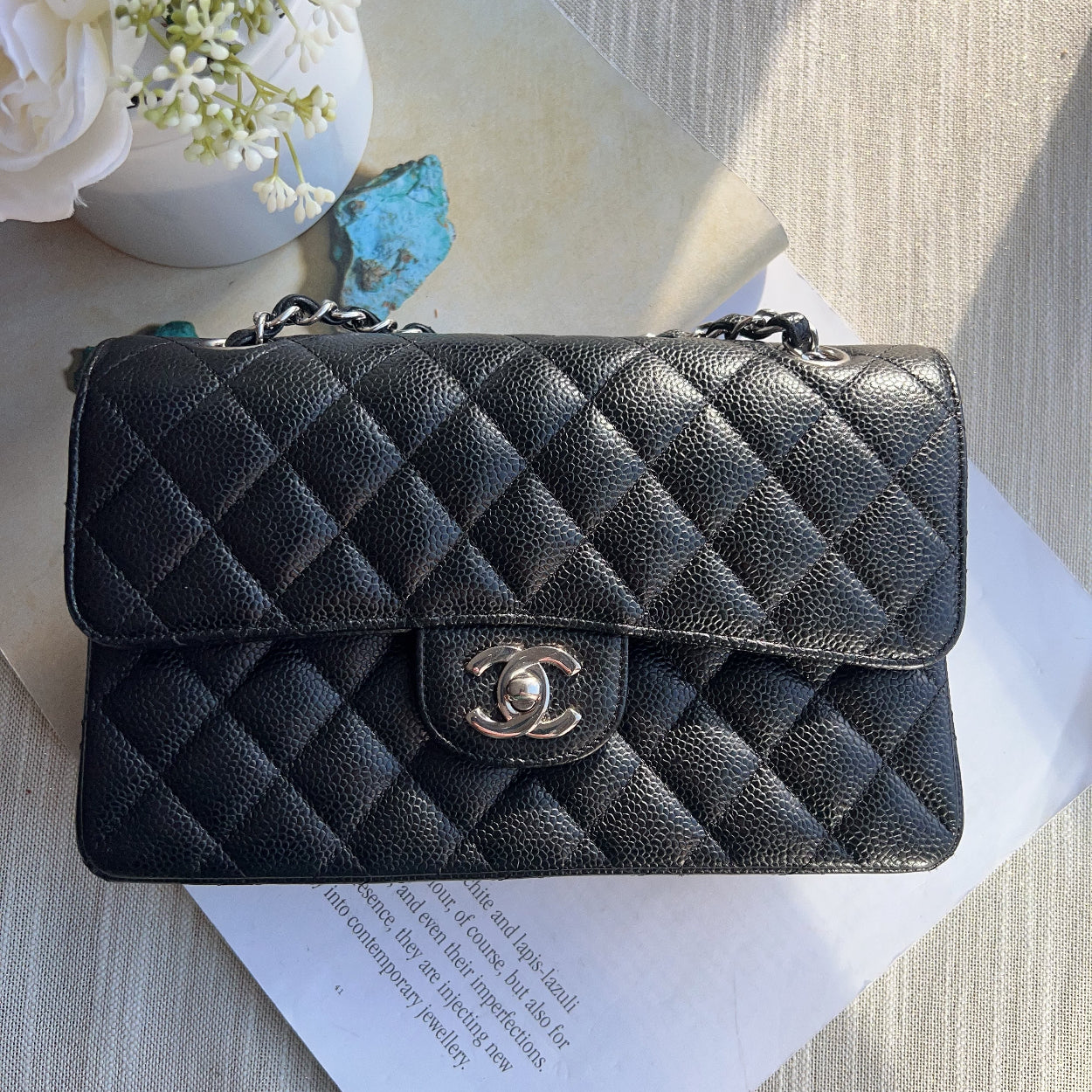 Black quilted Chanel wallet on a textured surface with flowers and paper.