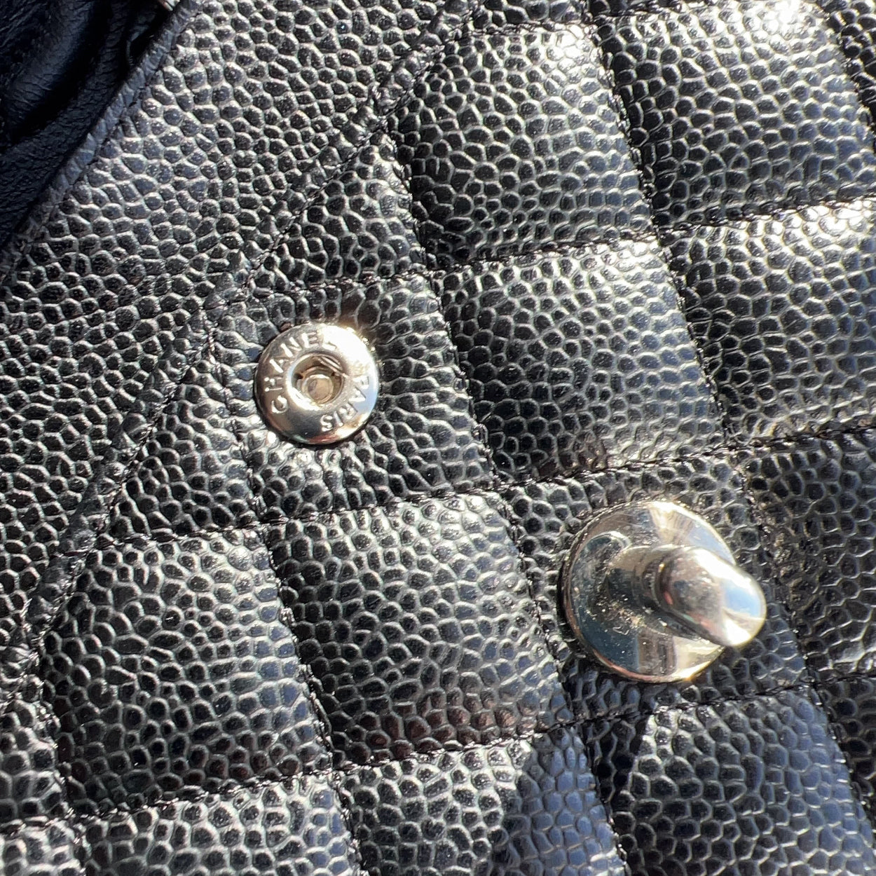 Close-up of a black textured handbag with metal buttons.