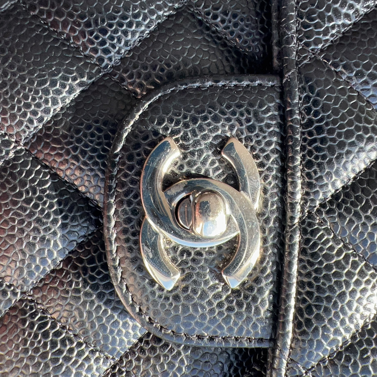 Close-up of a black quilted handbag with a silver logo on a white background