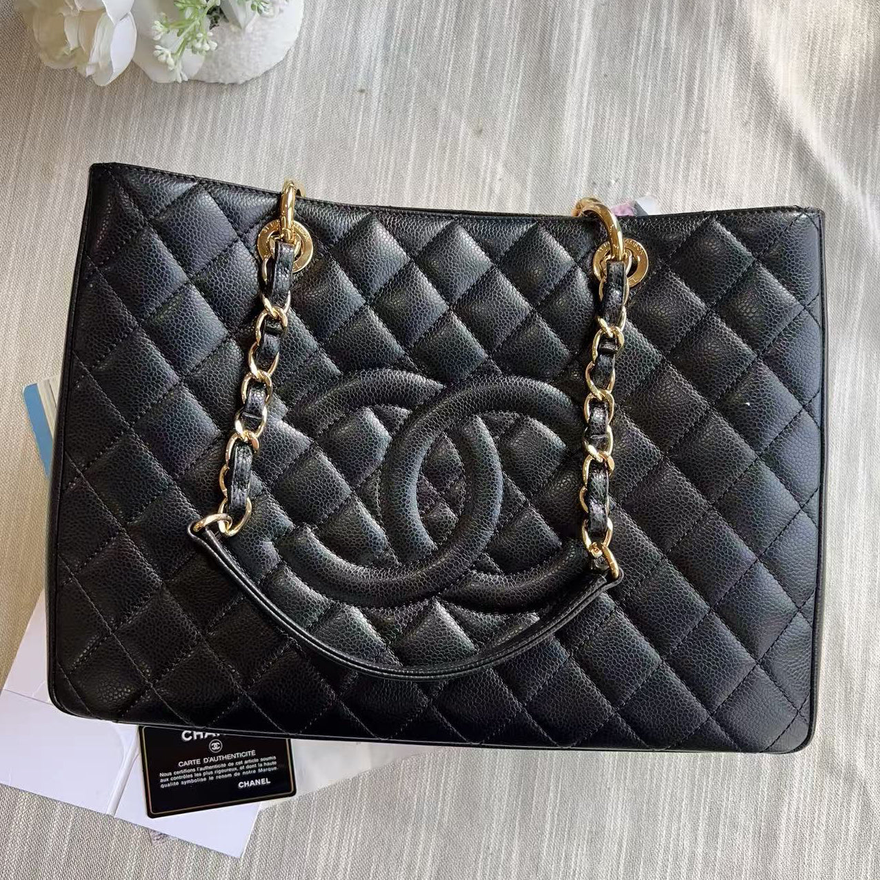 Black quilted handbag with gold chain on a textured surface with flowers and papers.