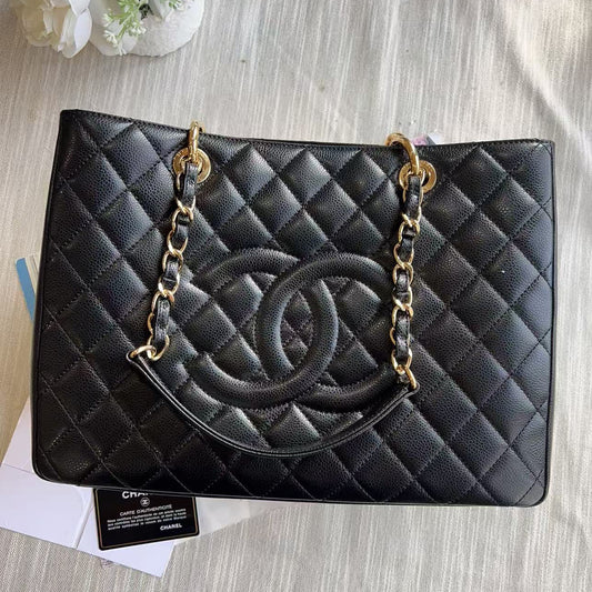 Black quilted handbag with gold chain on a textured surface with flowers and papers.