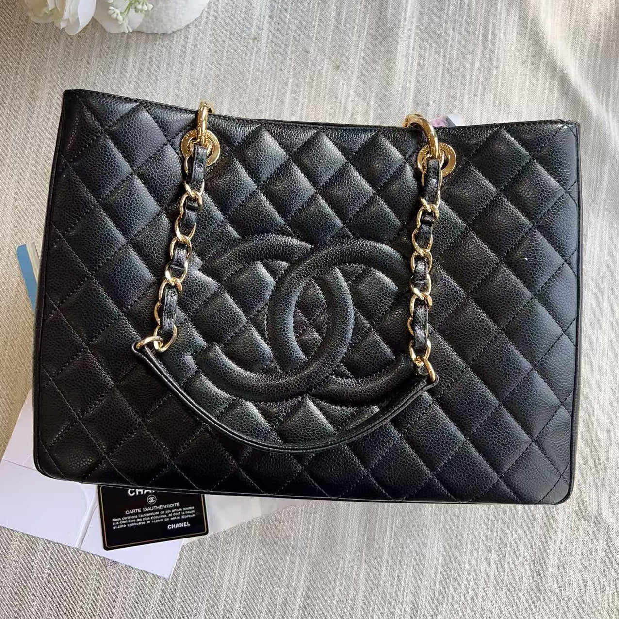 Black quilted handbag with gold chain on a textured surface with flowers and papers.