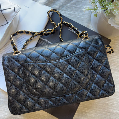 A black quilted caviar leather handbag with gold-tone chain strap details, styled on top of a black book over a light wood surface.